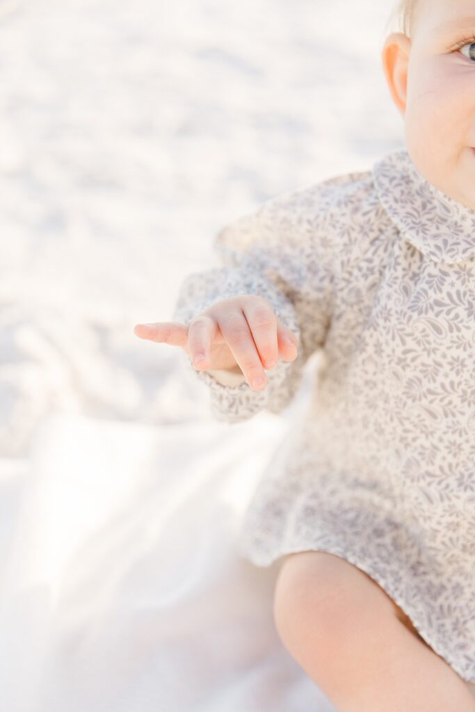A detail of a baby's hand while sitting on the white sand of Destin beach