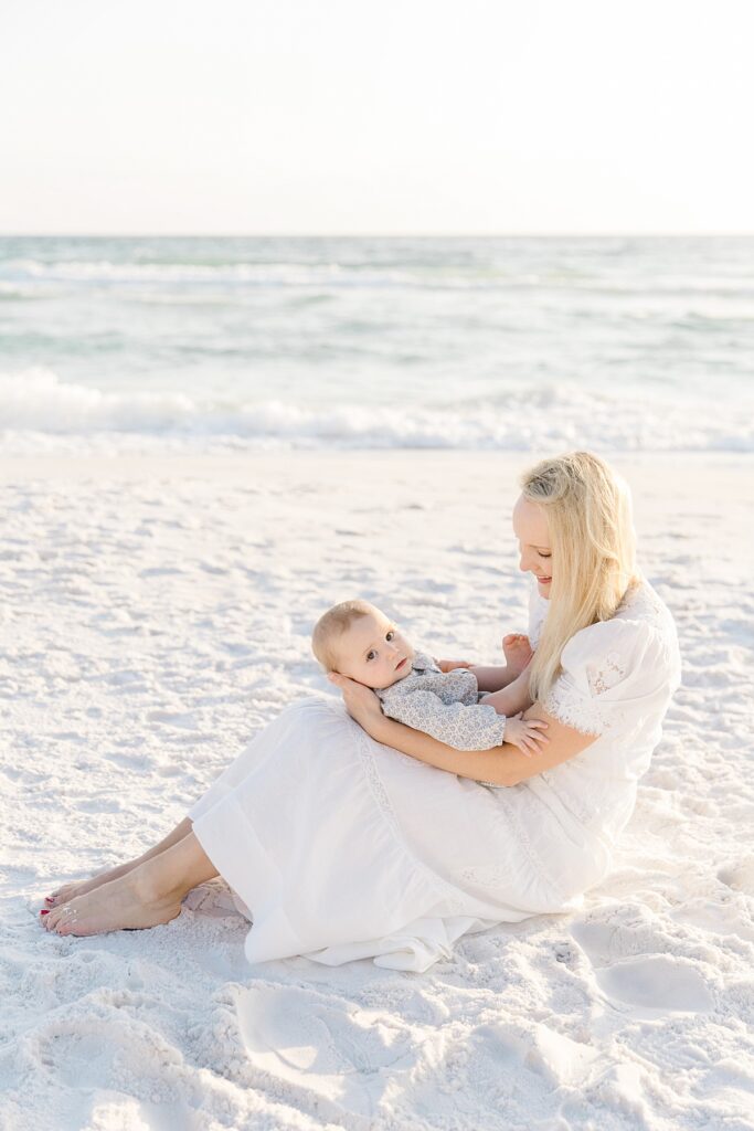 A mother sitting in the sand with her baby looking at the camera on Destin beach