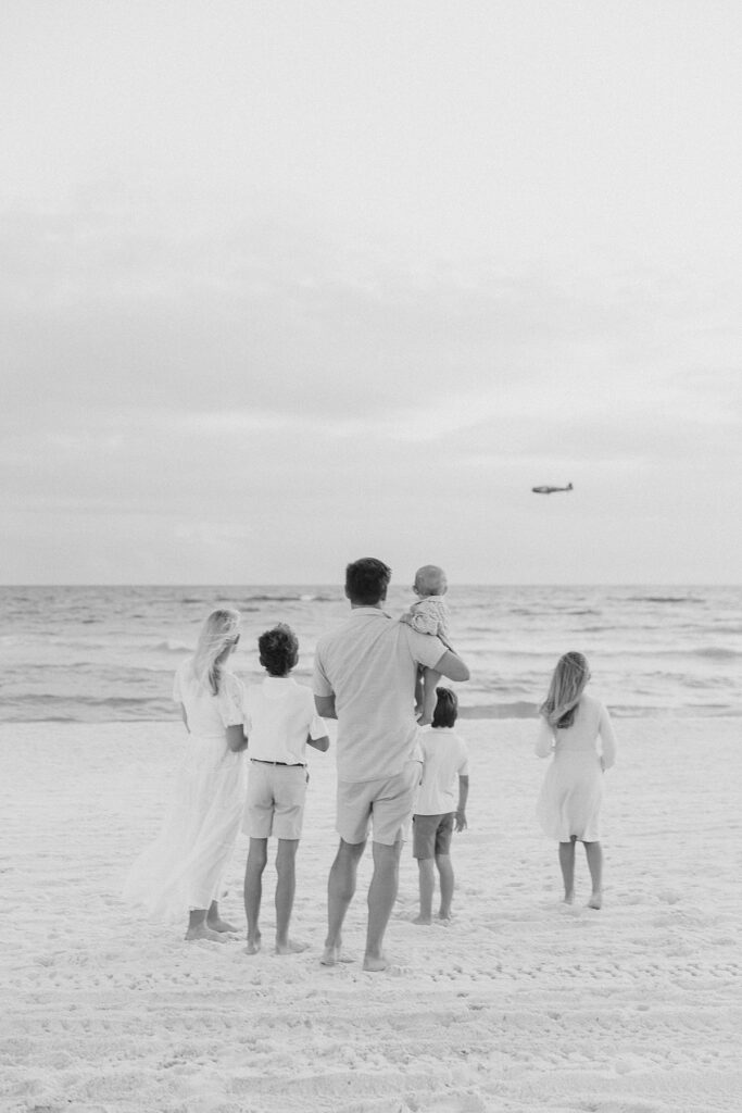 A family gathered together watching a low airplane fly by Destin beach